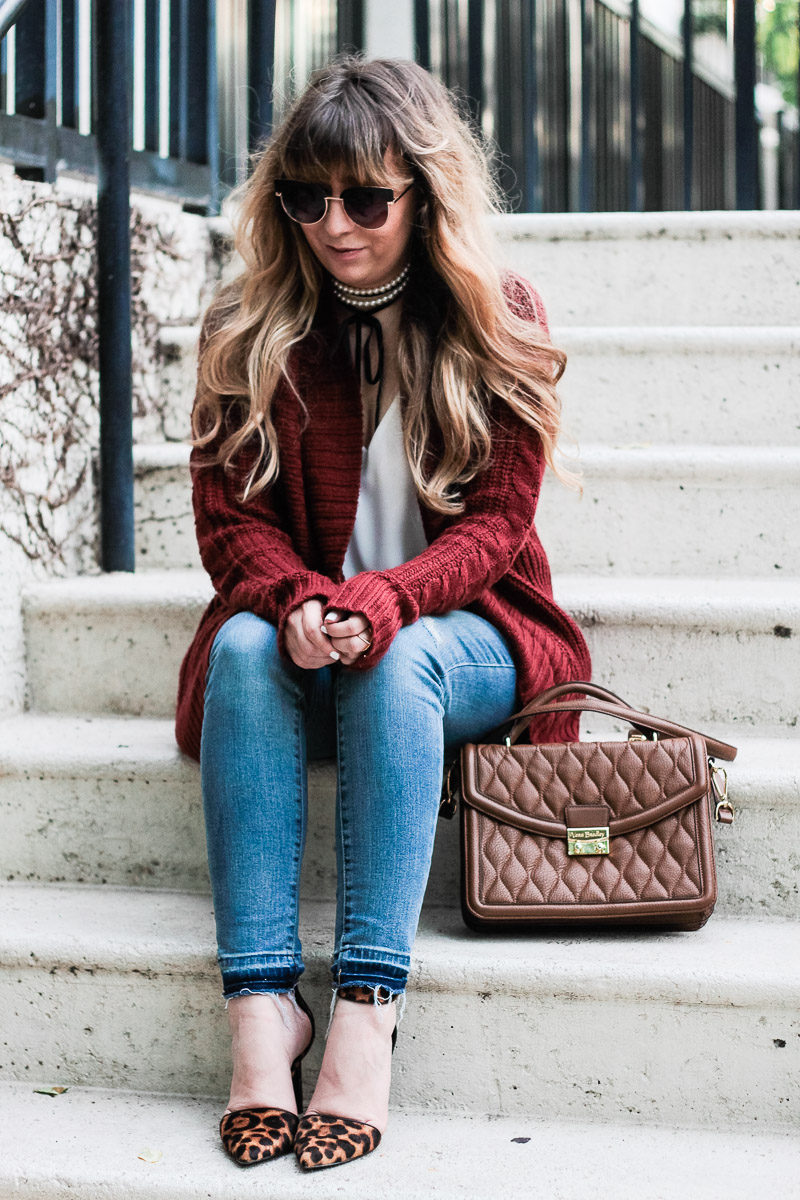 Miami fashion blogger Stephanie Pernas of A Sparkle Factor styles a cable knit cardigan with jeans and the Vera Bradley Lydia satchel in cognac 