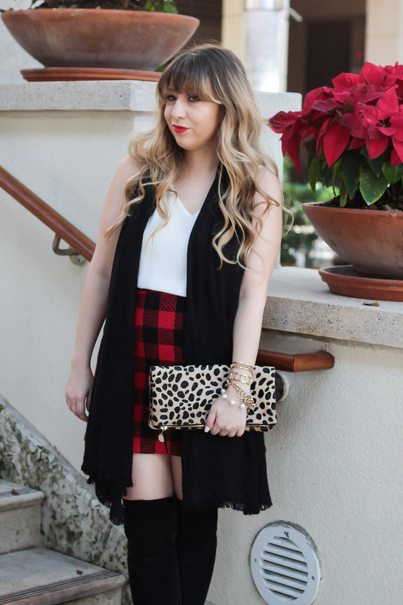 Fashion blogger Stephanie Pernas styles a red buffalo plaid skirt with a black scarf and over the knee boots for a Christmas outfit idea