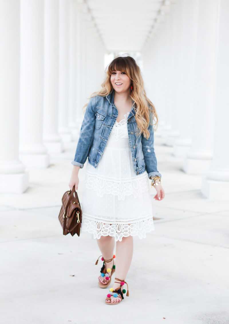 Miami fashion blogger Stephanie Pernas styles a white lace dress with jean jacket and pompom sandals for a cute spring outfit idea